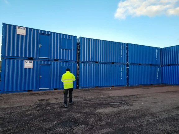 a stack of CHS containers with a person in a high-viz jacket inspecting them
