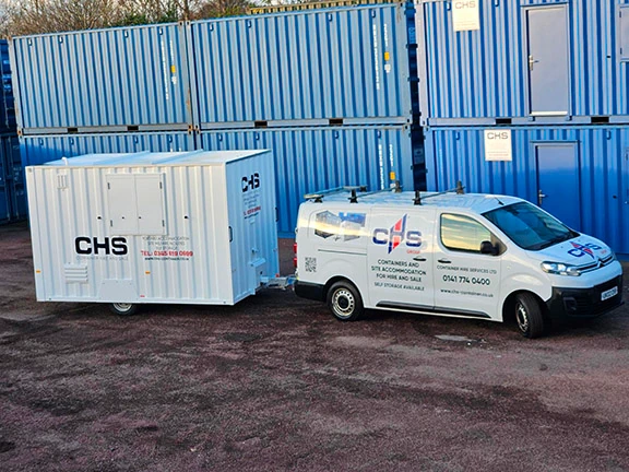 A mobile welfare unit being towed in front of a lighthouse.